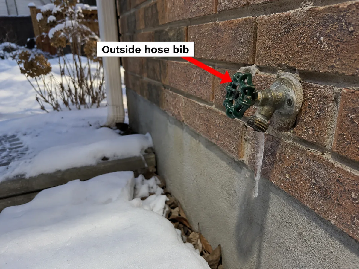 Outdoor hose bib on a brick wall with an icicle hanging from it