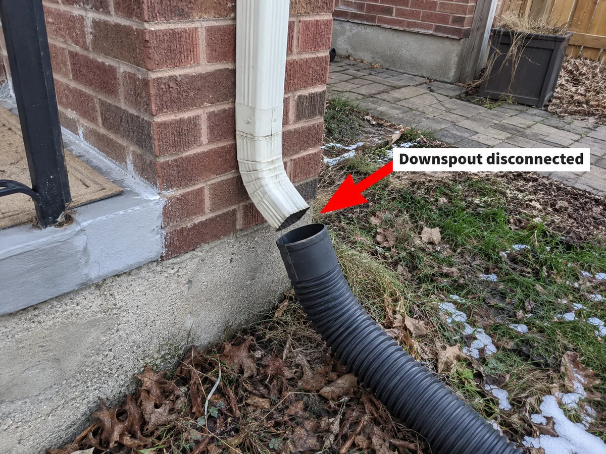Downspout on a brick house disconnected from the ground pipe with an extension hose